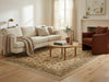 Load image into Gallery viewer, A styled living room scene featuring a cream bouclé sofa, a rust-brown accent chair, a round wooden coffee table, and a large beige and green patterned area rug on a light wood floor.