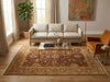 Load image into Gallery viewer, A styled living room featuring a large traditional oriental area rug with a red, beige, and gold floral pattern. The rug is styled with a glass-top coffee table, a cream-colored sofa, an orange armchair, and a potted plant in a warm, sunlit room.