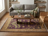 Load image into Gallery viewer, A styled living room scene featuring a rectangular area rug with a purple and beige floral pattern, placed under a wooden coffee table. The room includes a gray sofa, a woven armchair, and built-in wooden shelves in the background.