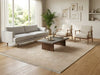 Load image into Gallery viewer, A styled living room featuring a light gray three-seater sofa, two cream armchairs with wooden frames, a dark wood coffee table, and a large beige patterned area rug on a light wood floor. The room is decorated with a potted palm, framed wall art, and built-in shelving.