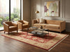 Load image into Gallery viewer, A styled living room scene featuring a tan three-seater sofa, two matching armchairs, a glass-top coffee table, and a large red and beige patterned area rug on dark wood flooring. The room has beige walls with paneling, a gold floor lamp, and a framed abstract painting.