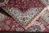 Load image into Gallery viewer, A close-up of a traditional patterned rug with a deep red field, beige borders, and blue floral motifs, showing folded sections and fringe.