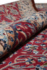 Load image into Gallery viewer, A close-up of a rolled traditional patterned rug showing its red, beige, and blue floral design against a matching flat section of the rug.