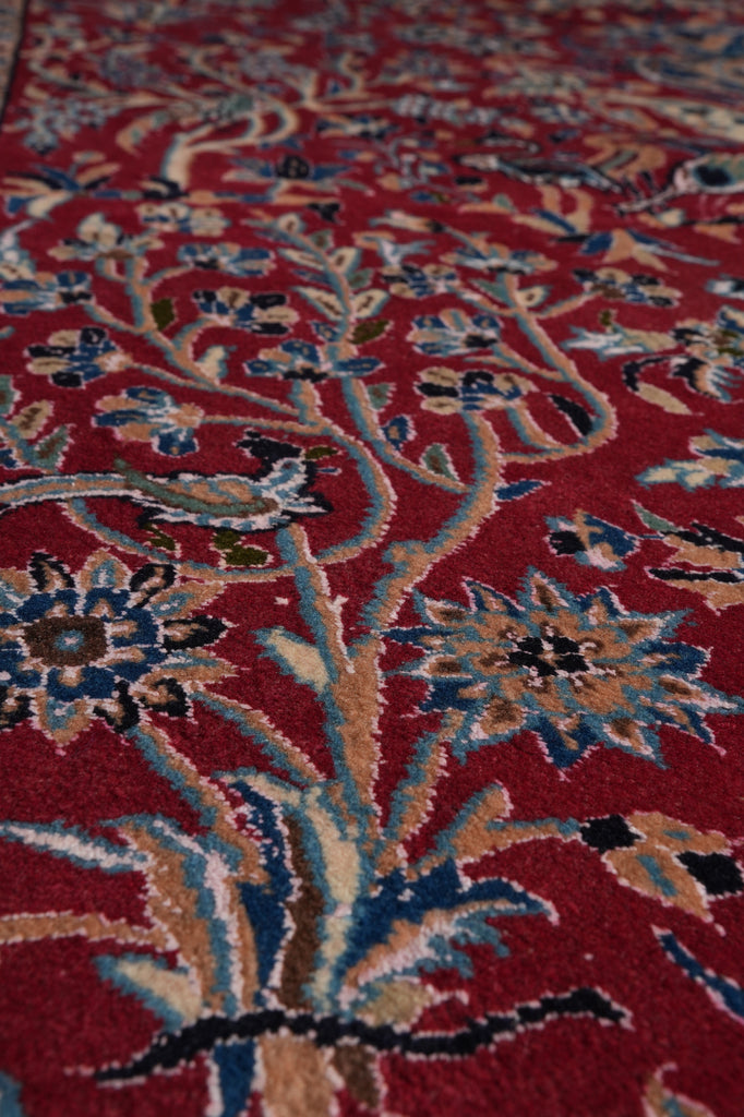 A close-up of a traditional patterned rug with a deep red background and intricate floral motifs in blue, beige, and black.