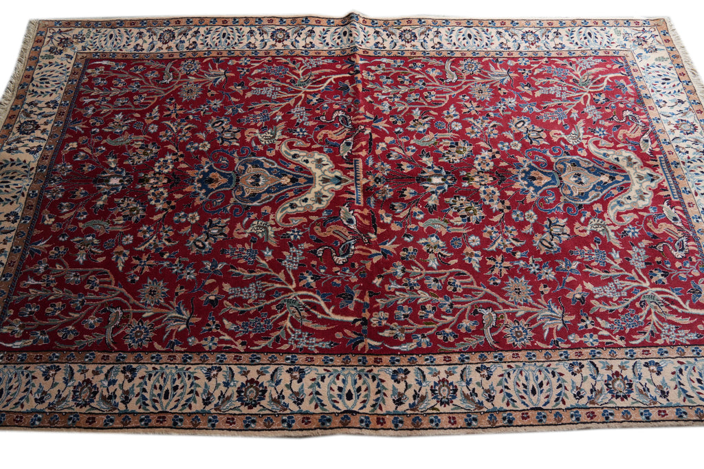 A large traditional oriental area rug with a deep red field, featuring intricate floral motifs in beige, blue, and green, with a detailed multi-colored border.