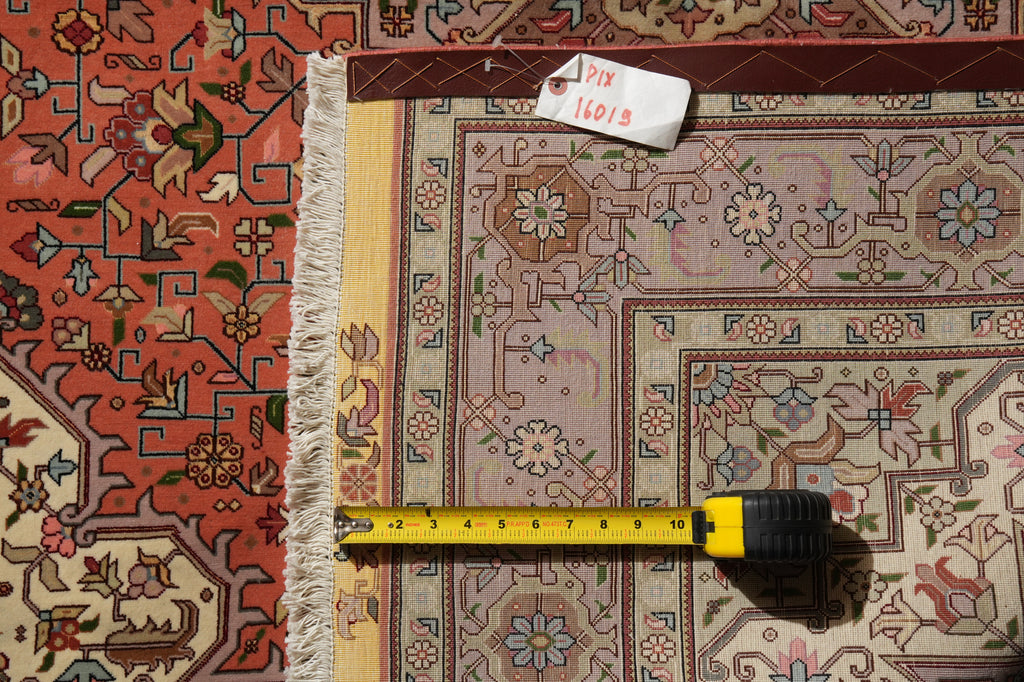 A close-up overhead view of a patterned area rug with a tape measure laid across the center and a small white tag reading 7x10ft on the upper edge, showing the rug's color and scale.