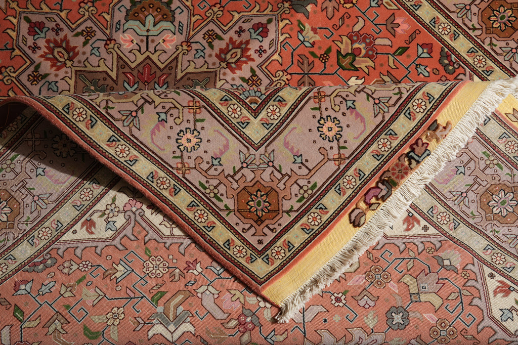 A close-up of a patterned area rug with a folded corner showing its cream and rust borders, featuring a central floral medallion and multicolored motifs.