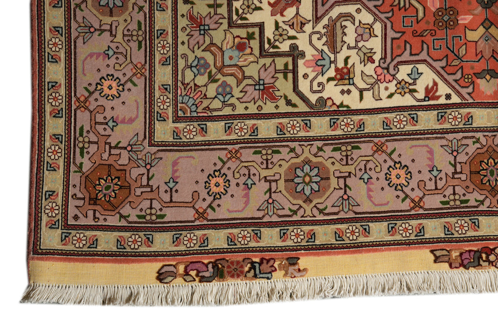 A close-up of an ornate patterned rug corner showing cream, pink, rust red, and brown floral motifs with a fringed edge on a white background.