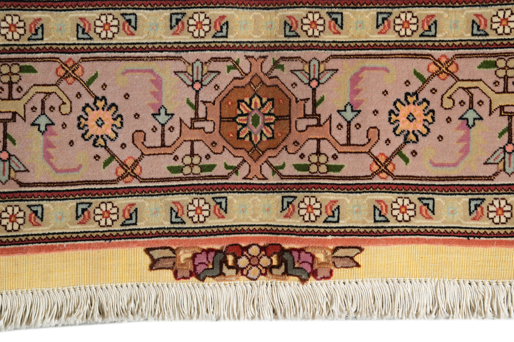 A close-up of a patterned rug showing a central medallion, floral motifs, and cream fringe along the bottom edge.