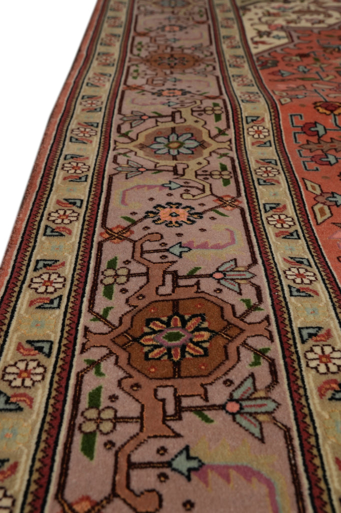 A close-up view of a traditional oriental rug showing its detailed pattern and color palette, featuring a dusty pink field with a central brown medallion and cream borders.