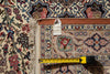 Load image into Gallery viewer, A close-up of a patterned area rug with a measuring tape laid across it to show the rug's dimensions. A small white tag is attached near the top edge.