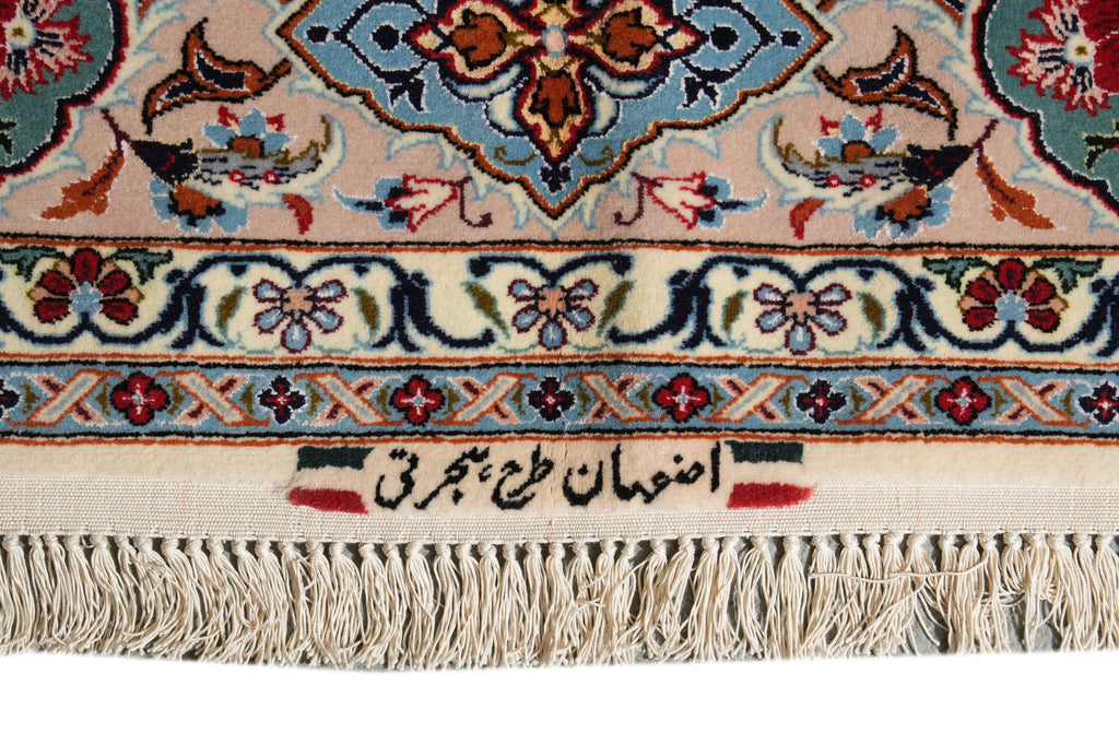 Close-up of an ornate patterned rug corner with cream fringe, featuring a beige field, blue and red floral motifs, and black Arabic calligraphy on a white background.
