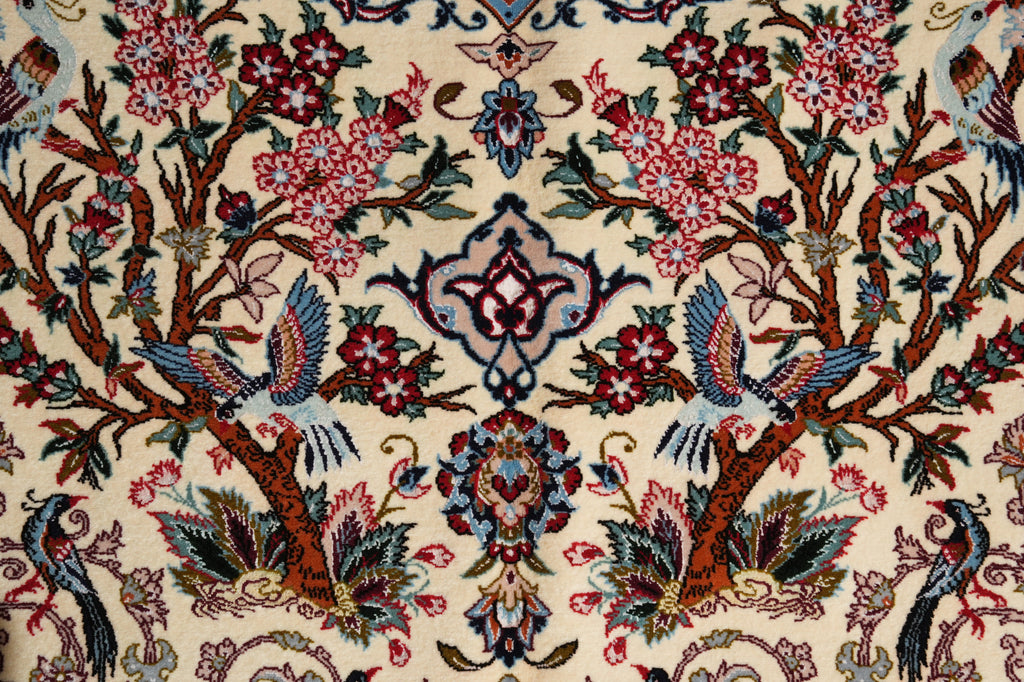 Close-up of an ornate patterned rug featuring a cream background with detailed floral motifs, birds, and tree branches in red, blue, green, and brown.