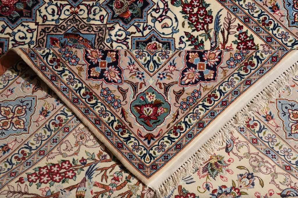 A close-up of an ornate Persian-style area rug with a cream base and intricate floral motifs in blue, red, green, and brown, featuring a folded corner that reveals the detailed pattern and cream fringe.