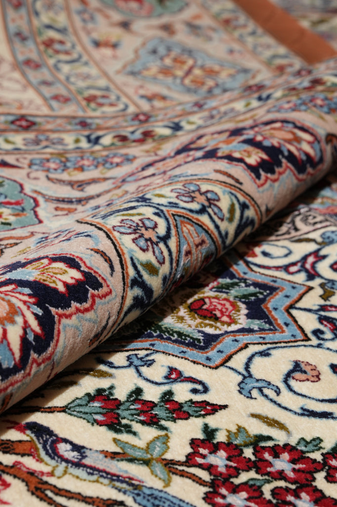 A close-up of a rolled section of an ornate patterned rug showing its detailed floral and geometric design in cream, blue, red, and brown tones.