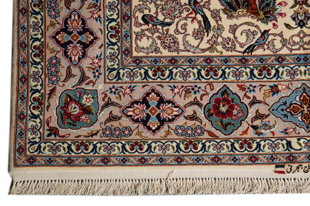 A close-up of an ornate Persian-style area rug showing the corner, detailed floral and bird motifs, cream background, and fringed edge.