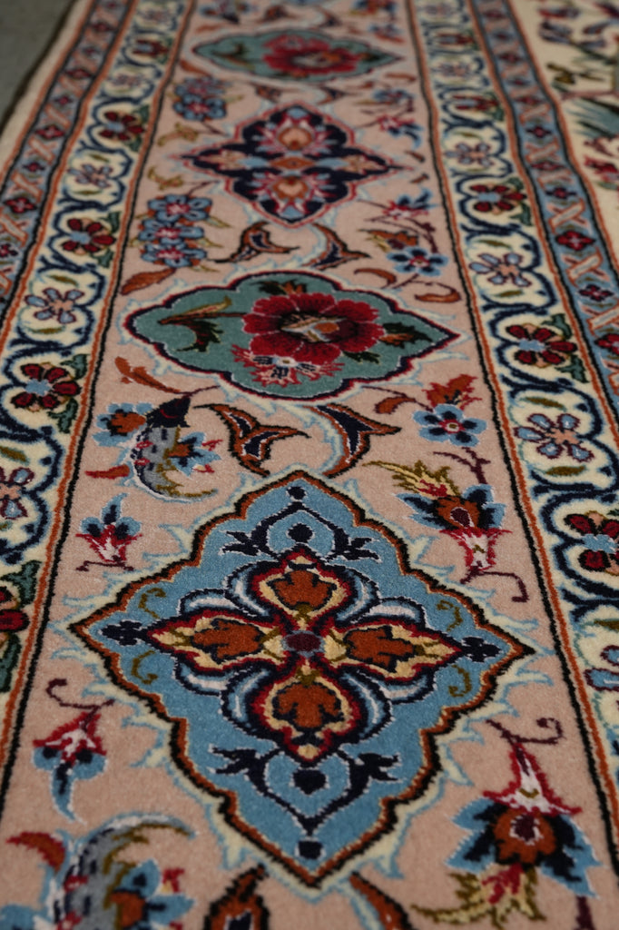 A close-up view of a traditional patterned area rug with a beige base, featuring a large blue medallion with red and orange floral details, surrounded by smaller floral motifs and a decorative border.