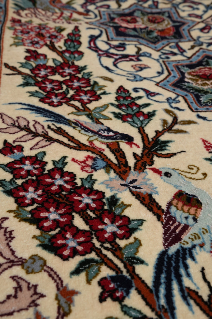 Close-up of a woven rug with a cream background and an ornate floral and bird pattern in red, blue, green, brown, and beige.