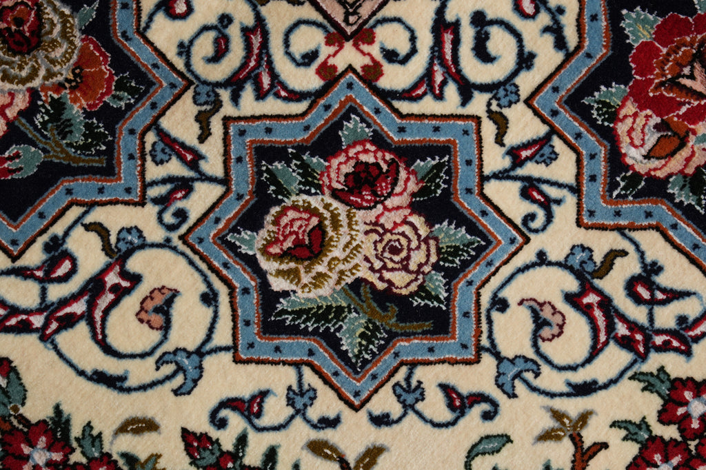 Close-up of a traditional patterned rug featuring a central floral medallion with red and pink roses, green leaves, and blue accents on an off-white background.