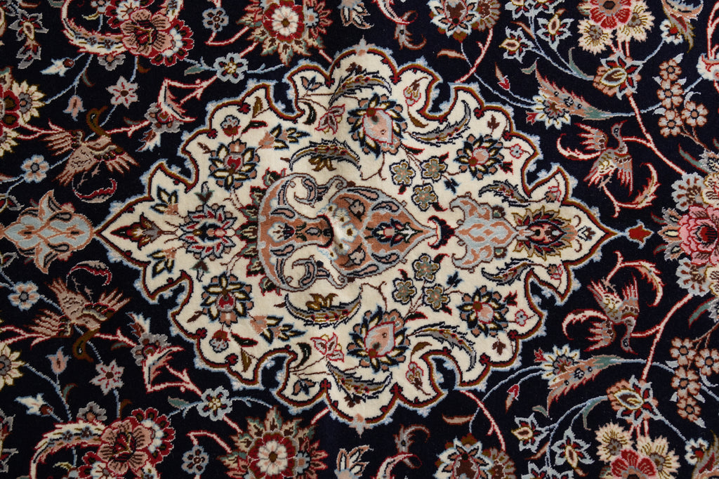 A close-up of an ornate Persian-style area rug featuring a large central medallion with intricate floral and bird motifs on a dark navy blue background.