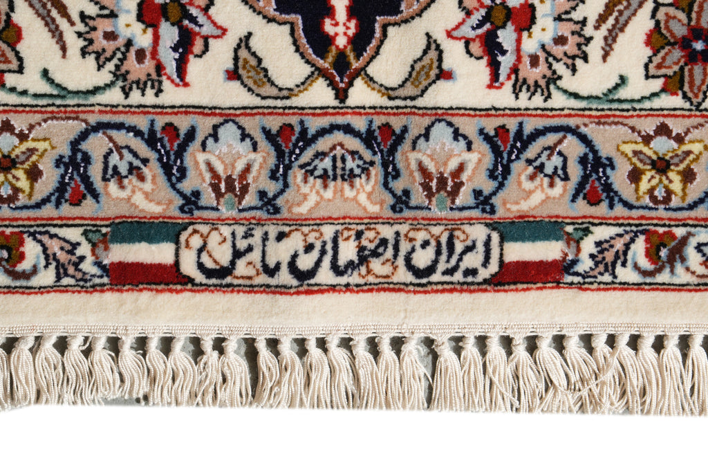 Close-up of an ornate patterned rug with cream, navy, red, and beige floral motifs, decorative bands, and a fringed edge.