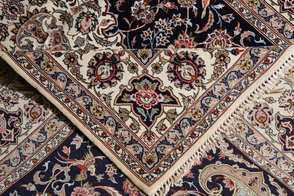 A close-up of an ornate Persian-style area rug with cream, navy, red, and gold floral motifs and fringed edges.