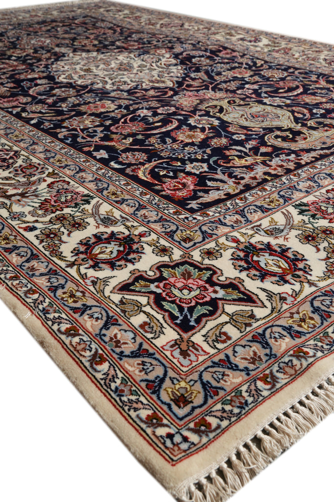 A traditional oriental area rug with an intricate floral and medallion pattern, featuring a dark navy blue field, cream borders, and red, green, and gold accents, shown on a white background.