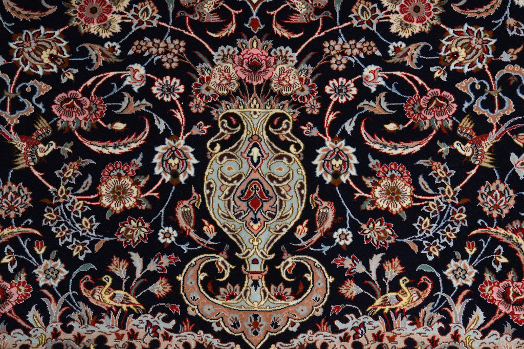 A close-up of an ornate woven textile or rug pattern with a central floral medallion and surrounding paisley-style motifs on a very dark navy or black ground. The design includes cream, beige, muted red, pink, and gold-toned details.