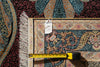 Load image into Gallery viewer, A close-up of a patterned area rug with a tape measure and price tag laid across it to show scale and details. The rug features an intricate Persian-style floral and scroll motif in deep teal, burgundy, gold, and cream.