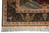 Load image into Gallery viewer, Close-up of an ornate patterned rug corner showing a dark navy field with intricate gold, beige, red, and blue floral motifs, plus a cream fringe along the bottom edge.