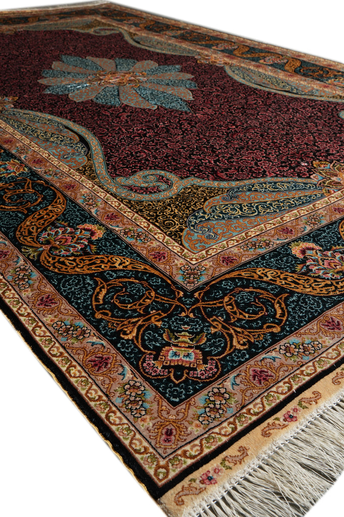 A close-up of an ornate area rug with a deep burgundy field, dark teal corner panels, and intricate beige, gold, and blue floral motifs, finished with cream fringe.