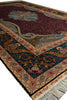 Load image into Gallery viewer, A close-up of an ornate area rug with a deep burgundy field, dark teal corner panels, and intricate beige, gold, and blue floral motifs, finished with cream fringe.