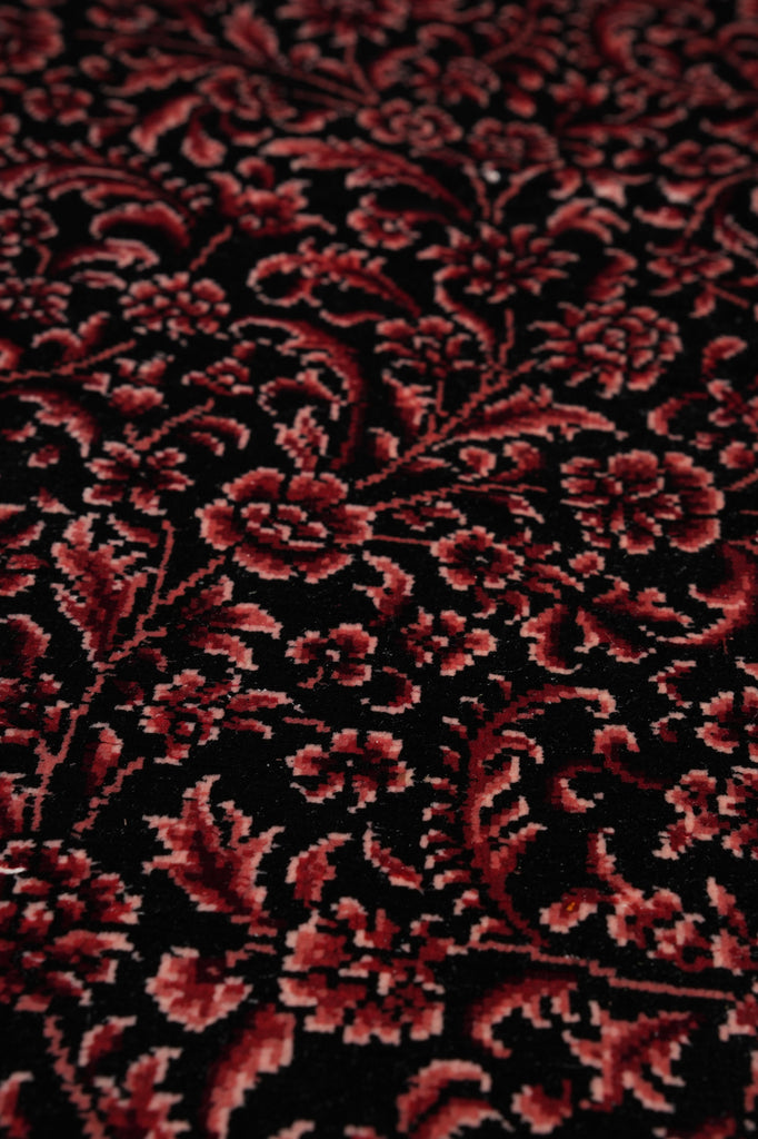 A close-up of a dark red and black floral patterned rug or textile with an ornate damask-style floral design.