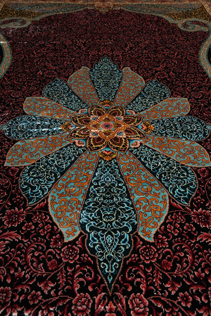 A close-up of an ornate Persian-style rug featuring a large central floral medallion in teal, gold, and red, surrounded by a dark red and black floral patterned field.