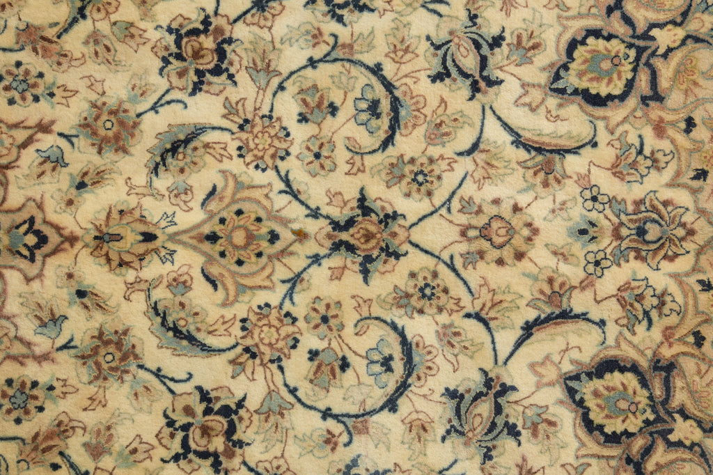 A close-up of an ornate floral patterned rug with a cream background and intricate designs in navy blue, beige, and light blue.