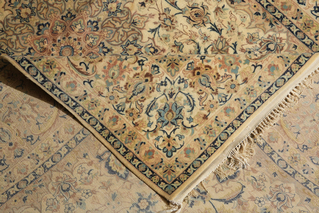 A close-up of an ornate area rug with a beige base and intricate floral motifs in blue, green, and rust tones, showing the corner and fringed edge.