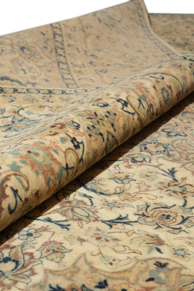A close-up of a rolled section of a traditional patterned rug showing its beige base with blue, brown, and muted orange floral motifs.