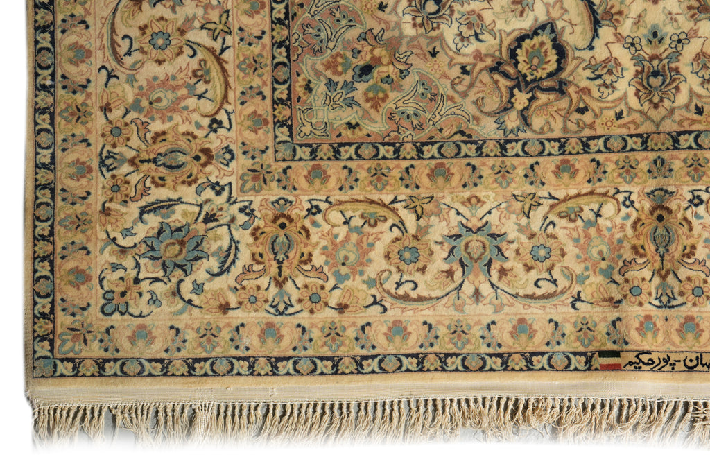 A close-up of an ornate Persian-style area rug showing its intricate floral and vine patterns, cream and beige base color, and fringed edge.