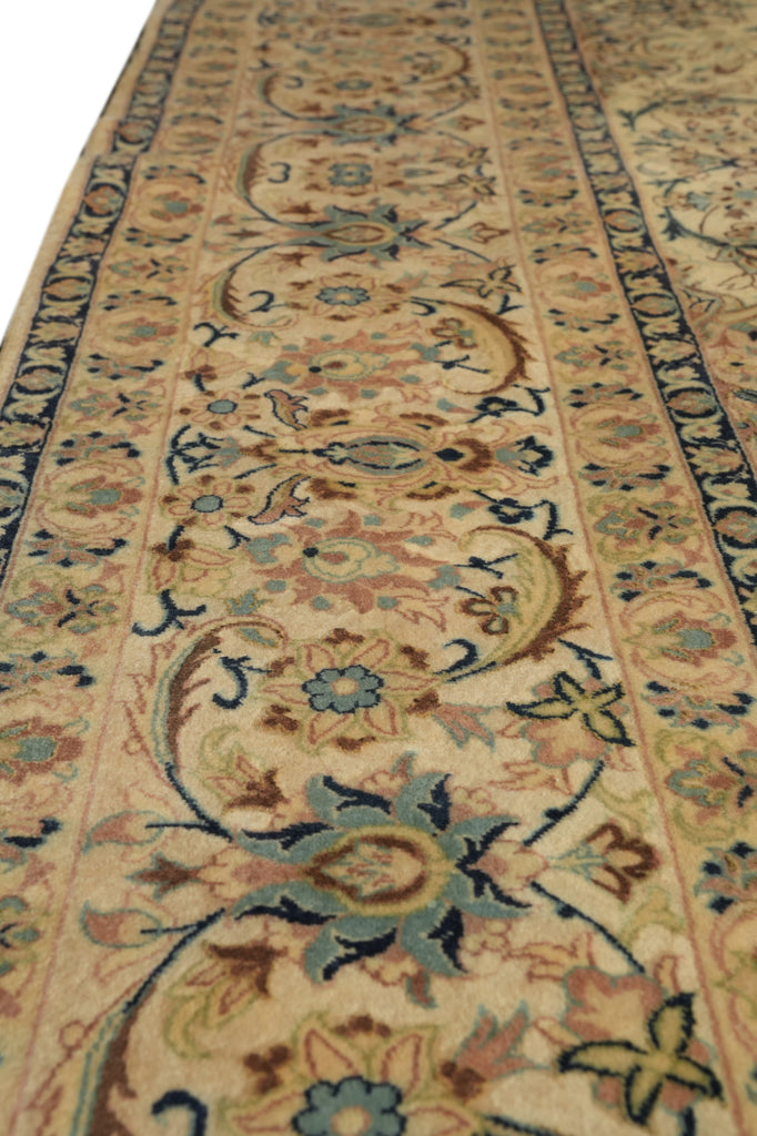 A close-up view of an ornate area rug with a traditional floral and vine pattern in beige, blue, brown, and muted green tones.