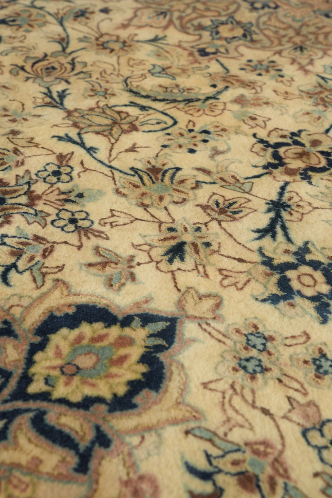 Close-up of an ornate floral area rug with a cream background and intricate patterns in navy blue, beige, brown, and muted green.