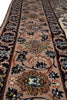 Load image into Gallery viewer, A close-up view of an ornate area rug with a traditional floral pattern. The rug features a central field of dusty pink and beige with dark navy blue borders and intricate floral motifs in blue, green, brown, and cream.