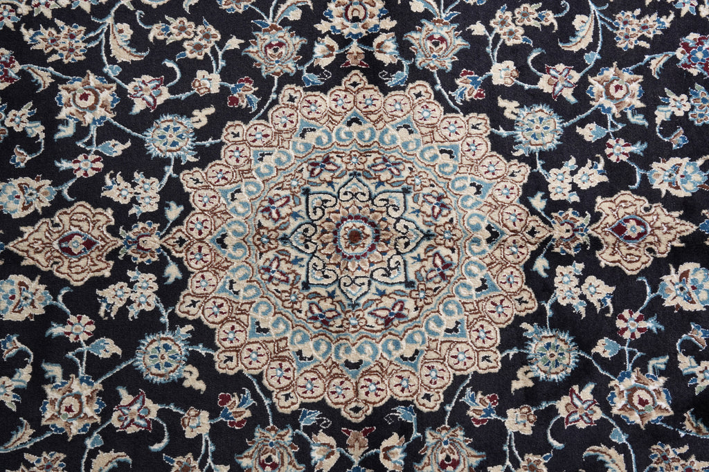 A close-up of an ornate traditional rug featuring a central medallion and surrounding floral motifs in beige, light blue, and red on a black background.