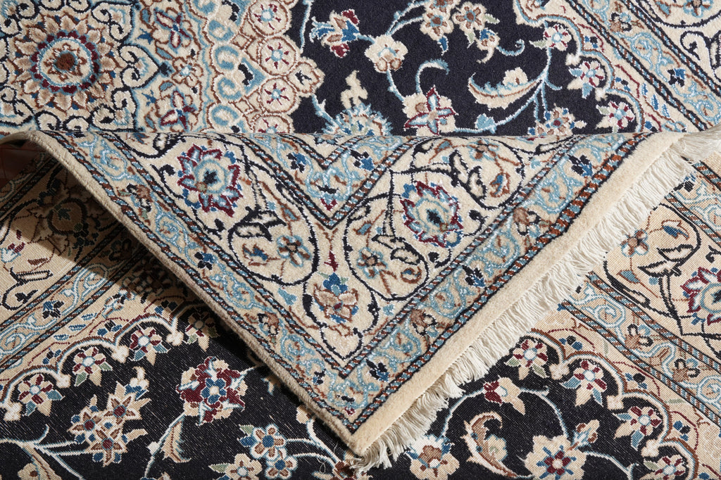 A close-up of a traditional patterned rug with cream, beige, light blue, and black floral motifs, showing the corner and fringe detail.