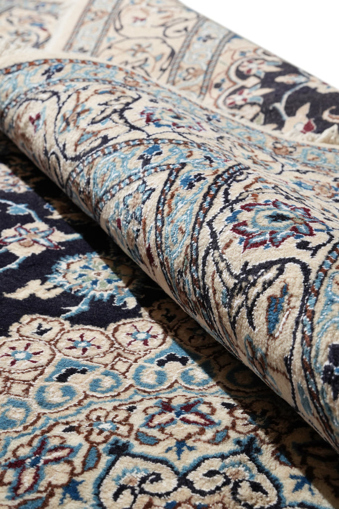 A close-up of a rolled area rug showing an intricate traditional pattern in beige, blue, brown, and navy tones.