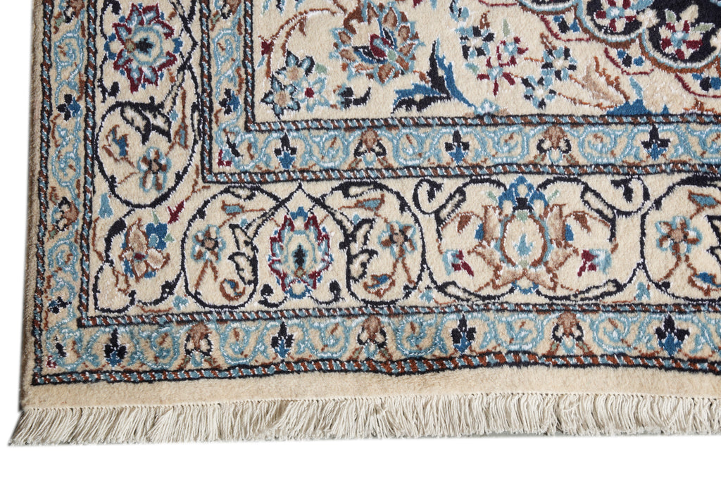 Close-up of a traditional patterned rug corner showing cream, blue, navy, and rust floral motifs with fringe along the bottom edge.