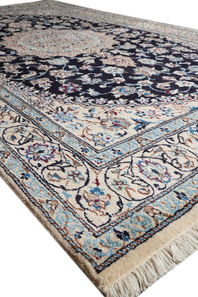 A traditional oriental area rug with a dark navy blue central field, beige borders, and light blue accents, shown from an elevated angle on a white background.