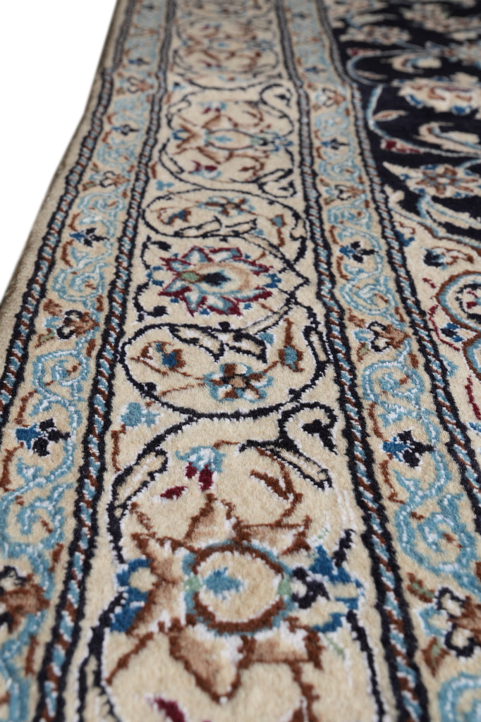 A close-up view of an ornate patterned area rug with a cream base, featuring blue, brown, and black floral motifs and borders.