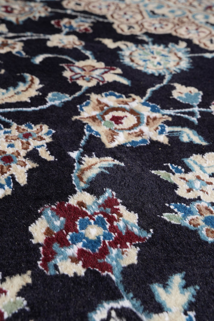 Close-up of a patterned rug with a dark navy background and floral motifs in cream, light blue, burgundy, and tan.