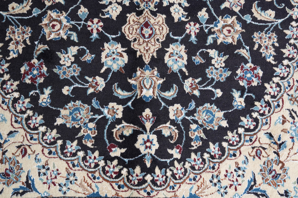 A close-up of an ornate traditional rug featuring a dark navy blue field with a cream border and intricate floral motifs in blue, beige, and red.