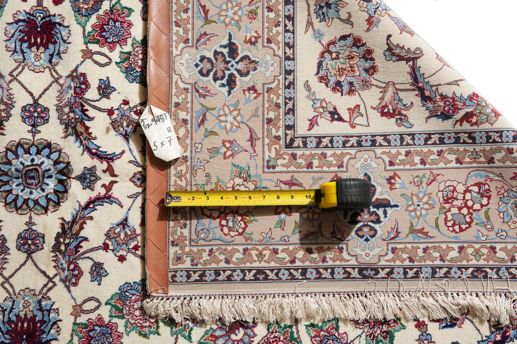 An ornate patterned area rug shown with a tape measure and price tag to indicate size and condition. The rug features a traditional floral and medallion design in beige, blue, red, and brown tones with a braided brown border and cream fringe.